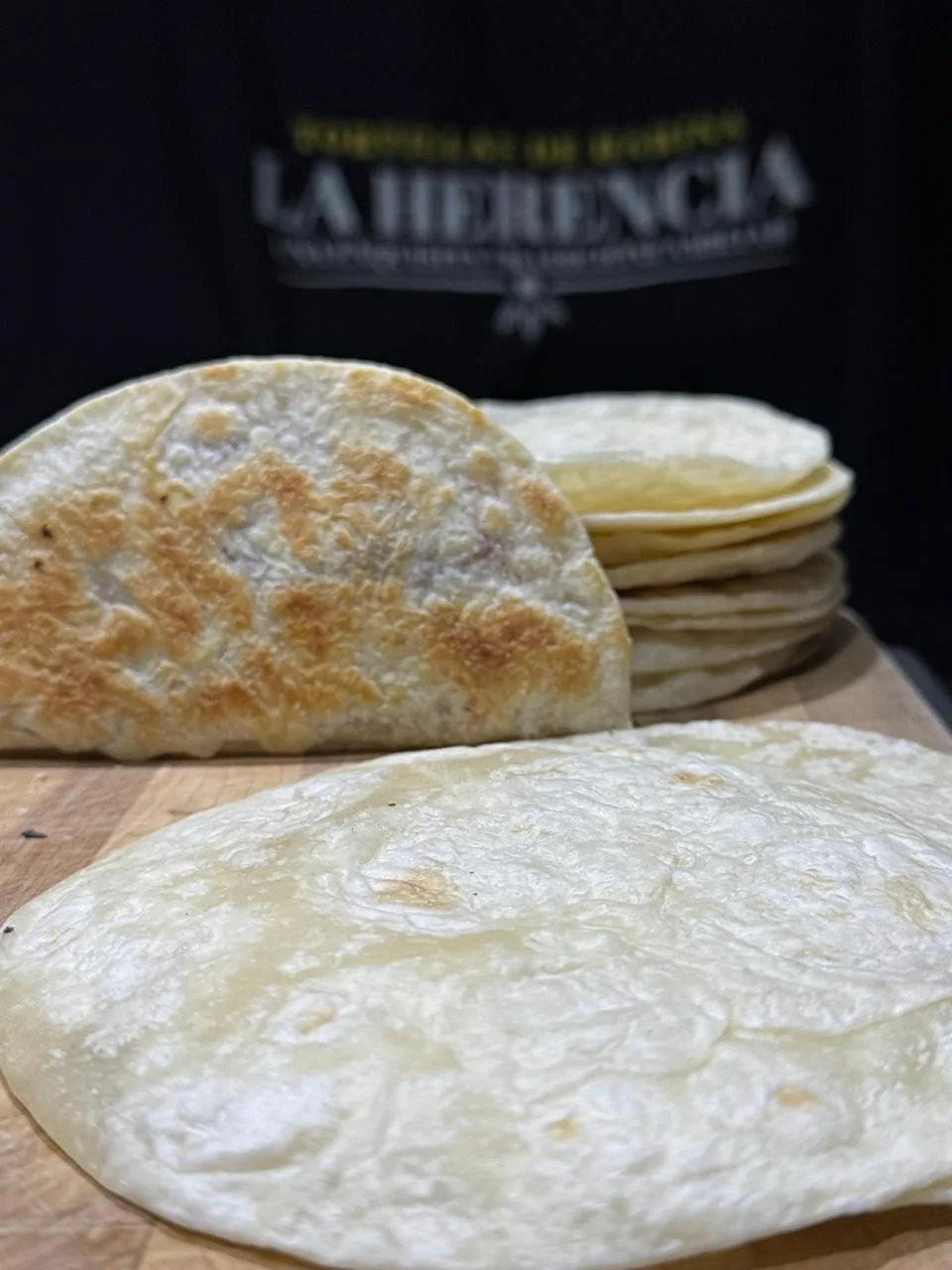 Tortilla de harina dorada y doblada junto a una pila de tortillas La Herencia